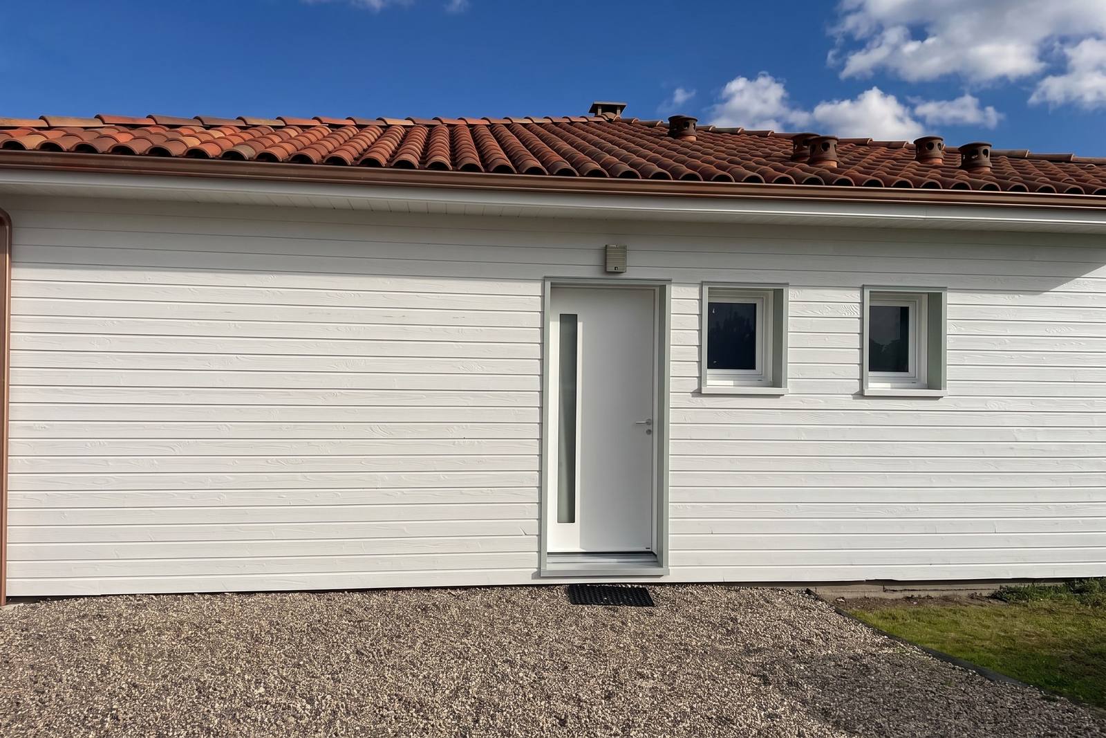 Entrée de la maison à ossature bois, bardage et menuiseries repeints en blanc cassé
