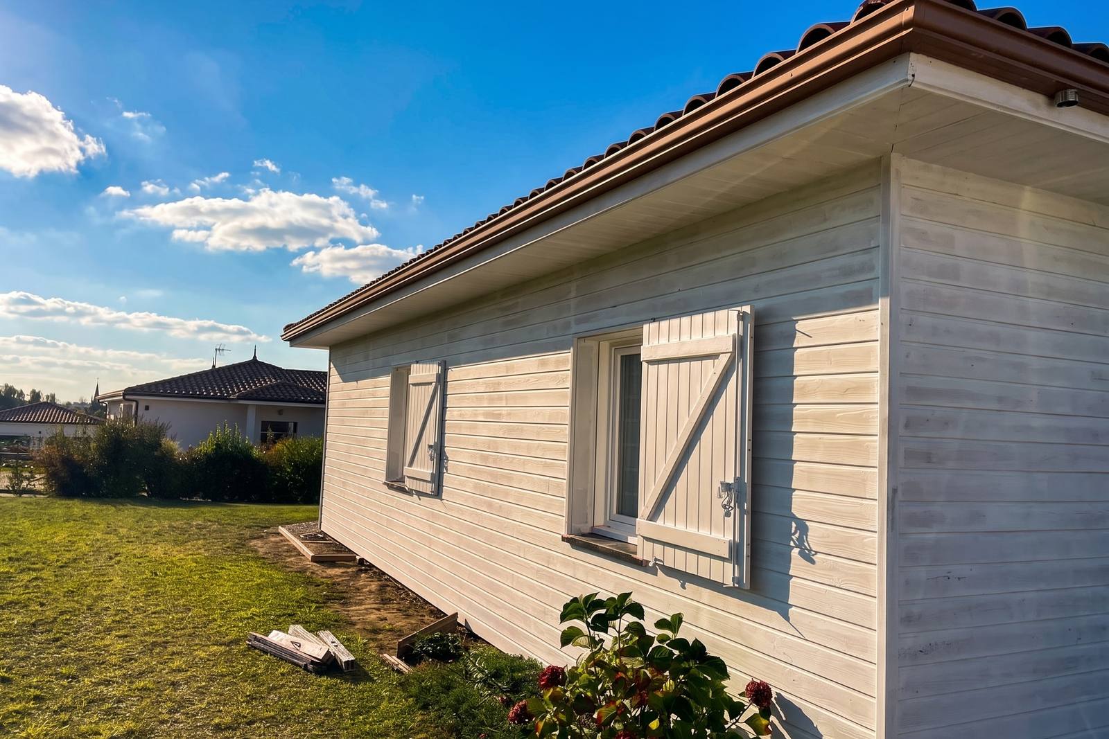 Volets bois vert pâle et bardage blanc cassé d’une maison à ossature bois rénovée